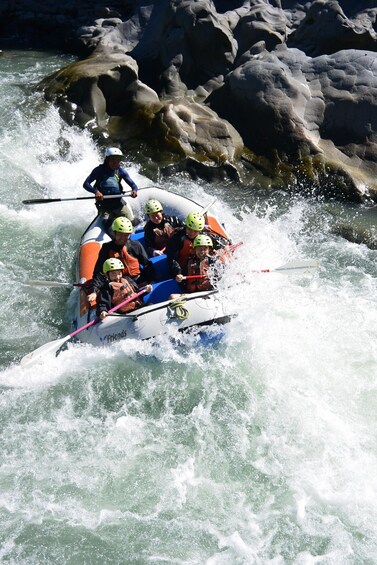 A group of people in a white inflatable raft navigating through a river with rapids, surrounded by large rocks. 2