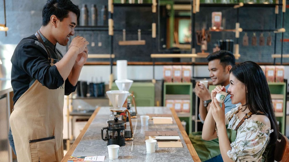 A barista preparing coffee at a counter with customers seated. 1