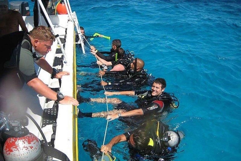 Divers in black wetsuits with helmets and fins, preparing to enter the water from a boat. 4