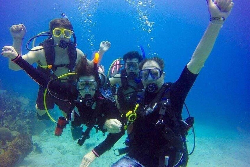 Three scuba divers underwater with their arms raised, surrounded by clear blue water and marine life. 3
