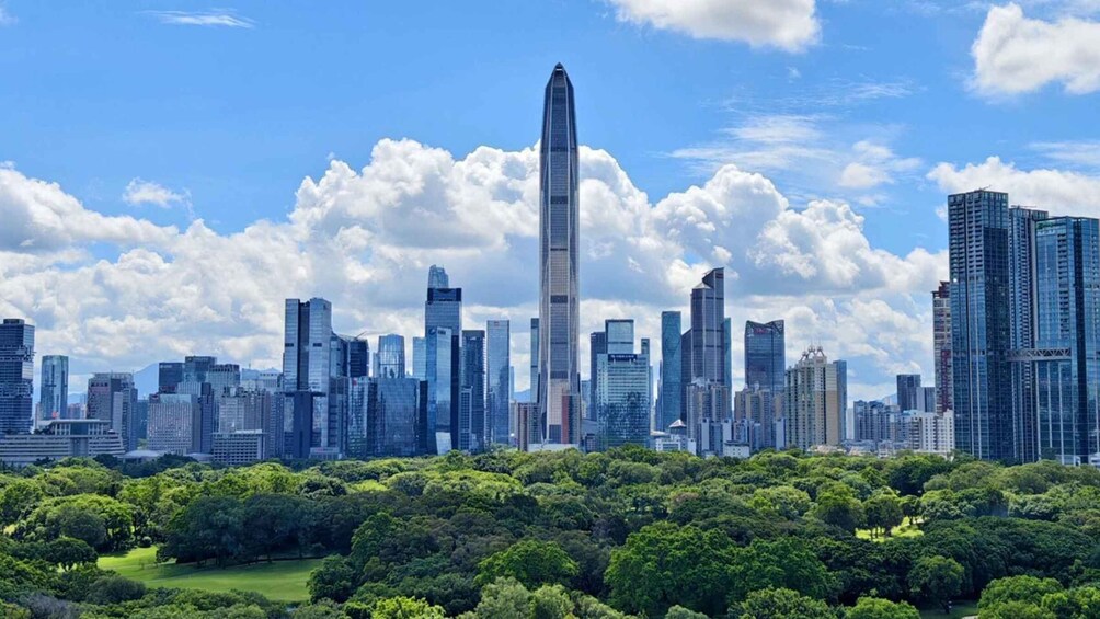 A city skyline with a prominent skyscraper, surrounded by other high-rise buildings and a park with dense green trees. 2