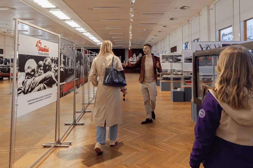 An indoor exhibition with people walking, a poster with text, and display cases. 5