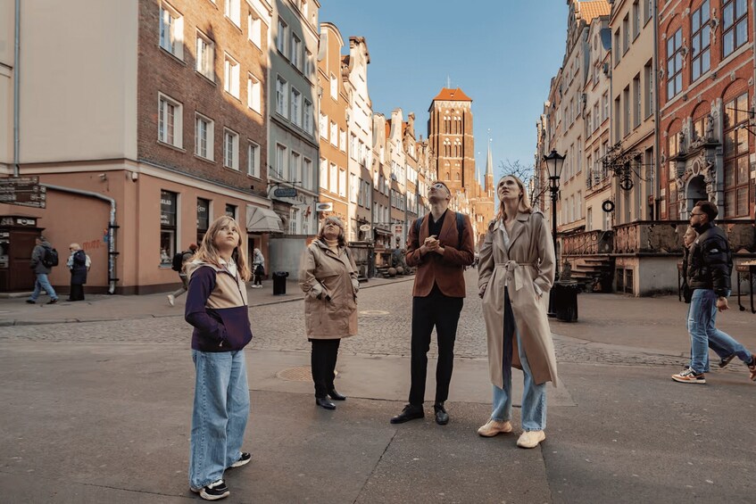 A group of people standing on a cobblestone street in a historic European city with old buildings and a church tower in the background. 2