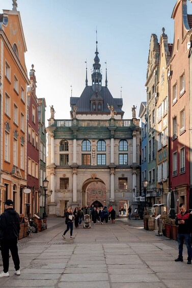 A historic building with ornate architecture, a cobblestone square, and people walking. 1