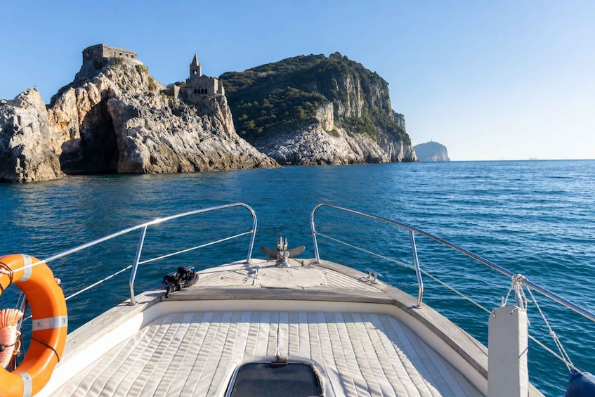 A boat's deck with a lifebuoy, a small cabin, and a rocky island with a tower in the background. 1