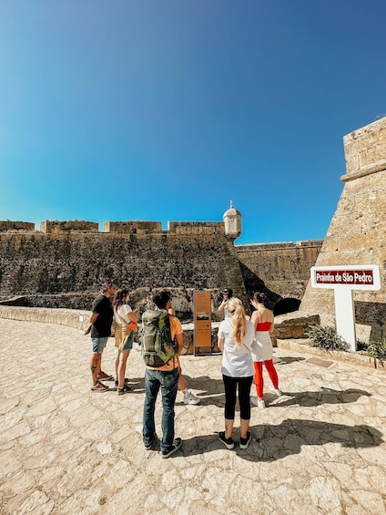Tourists at a historical site with a sign reading 'Praia de São Pedro.' 1