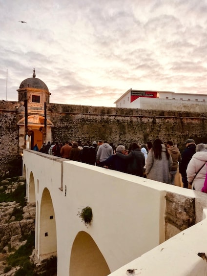 A historical site with a crowd of visitors, a watchtower, and a museum sign. 4