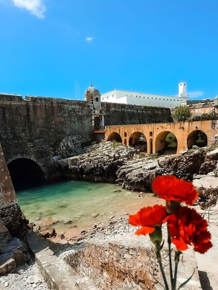 A coastal stone bridge, clear turquoise water, and a white building with a tower. 2