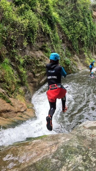 A person running through a river with rapids, surrounded by greenery and rocky terrain. 2