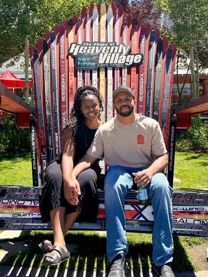 Two people sitting on a bench with a sign that reads 'Heavenly Village' and 'lake tahoe' in the background. 3