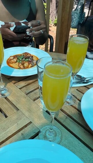 A table with a plate of food, two glasses of a yellow beverage, and a person using a smartphone. 4