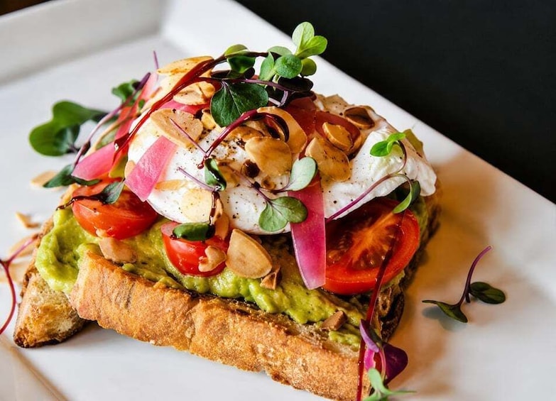 A sandwich with avocado, tomato, and egg on a slice of bread, garnished with microgreens and radish. 1