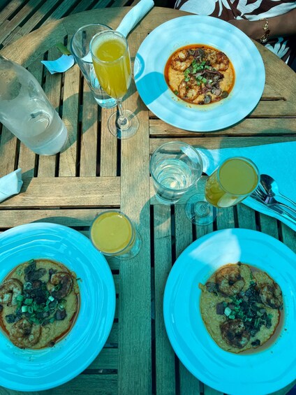 A wooden table with plates of food, glasses of a yellowish drink, and a clear glass. 2