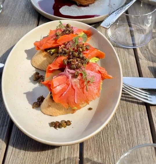 A plate of food with salmon, capers, and herbs on a wooden table. 2