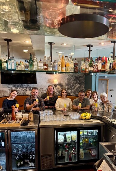 A bar with a variety of liquor bottles and glasses, a refrigerated display case, and a group of people seated at the bar. 3