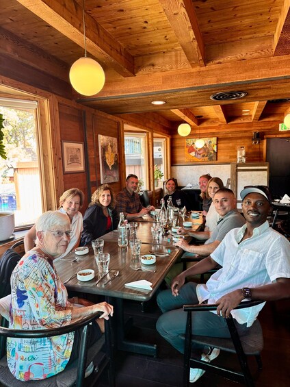 A group of people seated around a wooden table in a restaurant with wooden beams on the ceiling and framed artwork on the walls. 4