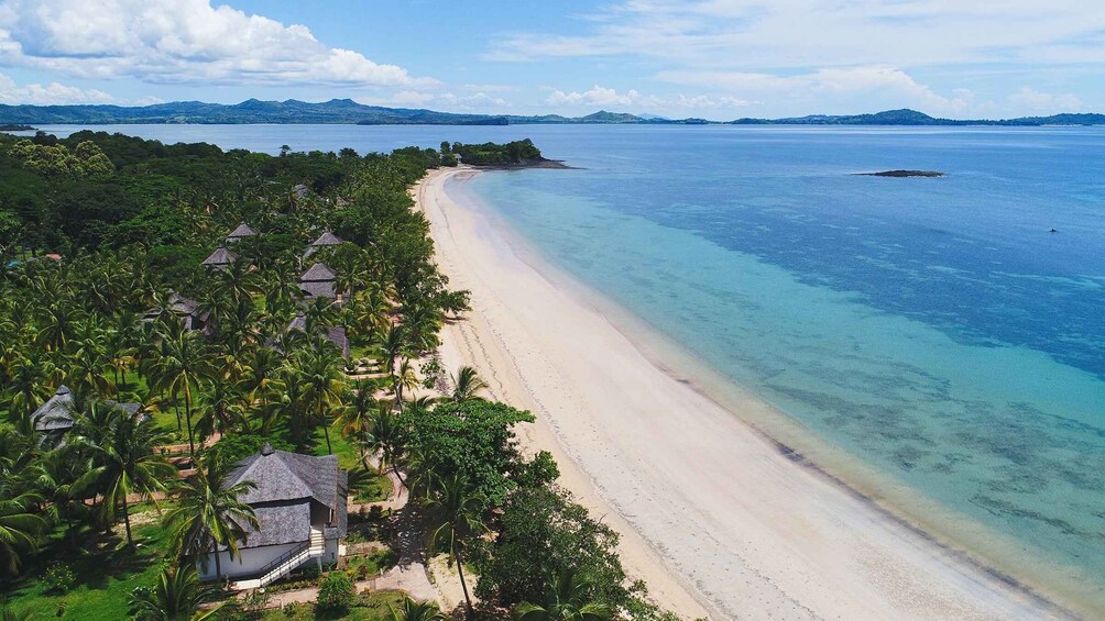 A tropical beach with clear waters, palm trees, and a distant mountain range. 5