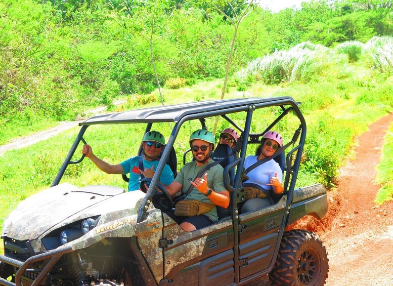 A group of people in a rugged off-road vehicle on a dirt path surrounded by greenery. 1