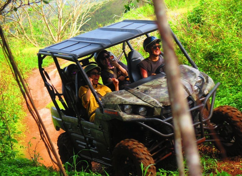 A group of people in a four-wheeled vehicle with a camouflage pattern, driving on a dirt path surrounded by greenery. 5