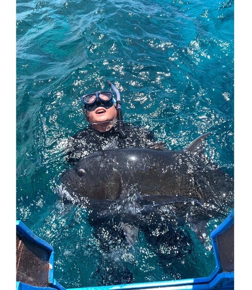 A person in a blue wetsuit holding a large fish in clear blue water. 2