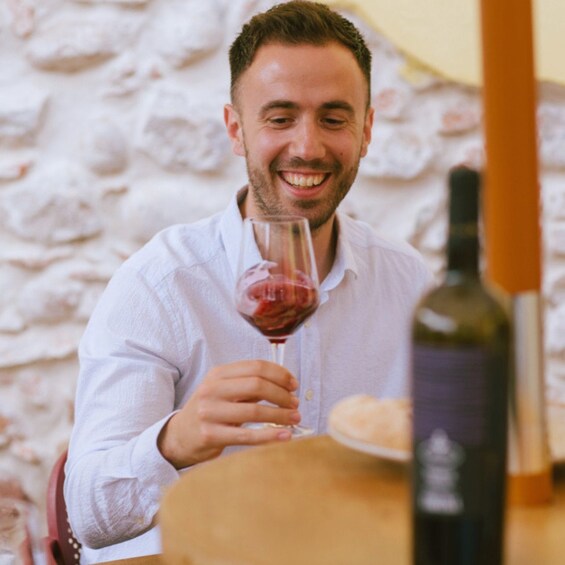 A person holding a wine glass at a table with a bottle of wine and a plate of food. 5