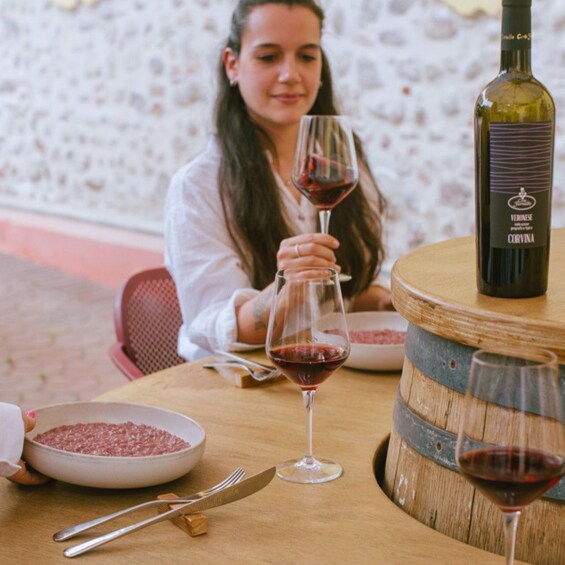 A person seated at a table with a bottle of wine, glasses, and a bowl of grapes. 2