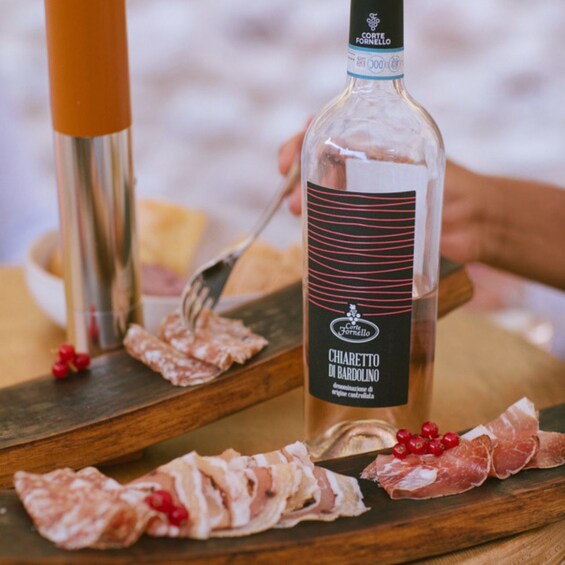 A bottle of Chiavetto di Bardolino on a wooden board with sliced meats and red berries. 3