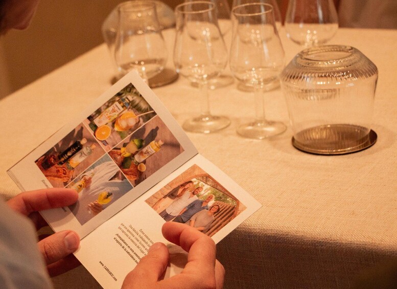 A person holding a menu with food images and a table with wine glasses and a glass jar. 4