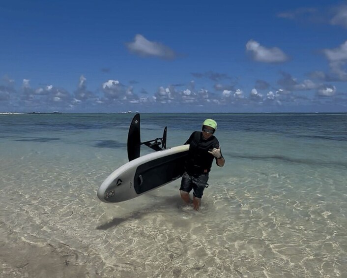 A person carrying a surfboard on a beach with clear water and a distant boat. 3