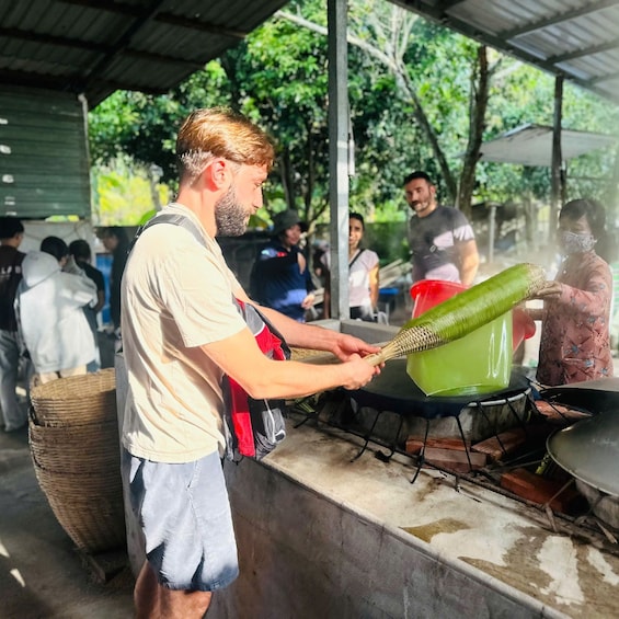 A person preparing food outdoors, possibly grilling, with a covered area and trees in the background. 3