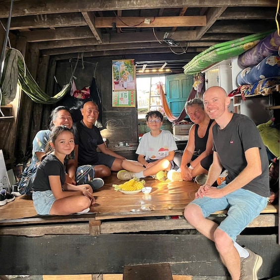 A group of people sitting around a wooden table in a rustic setting with hammocks and colorful pottery in the background. 2
