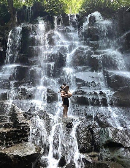 A waterfall with multiple cascades and a person standing in the foreground. 1