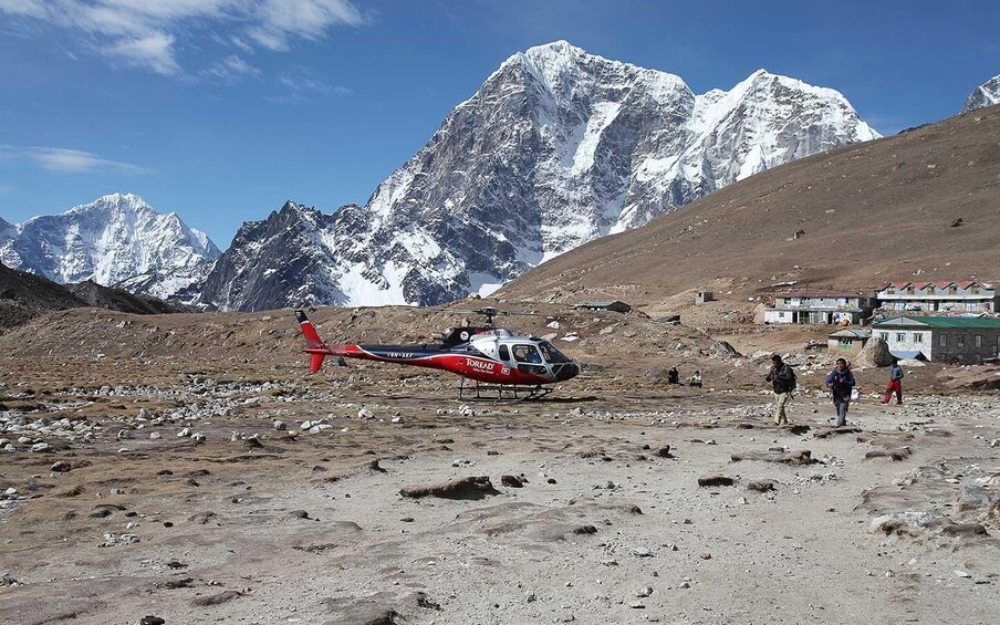 A red and white helicopter parked on a rocky terrain with snow-capped mountains in the background. 3