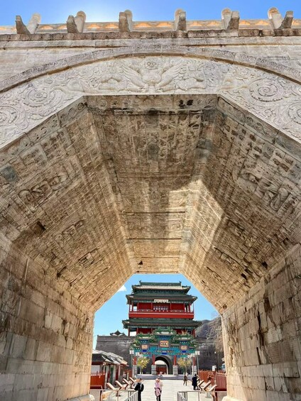 A stone archway with intricate carvings and a traditional Chinese building in the background. 3