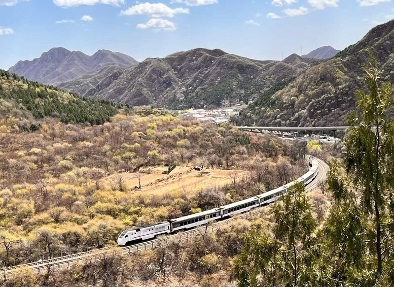 A high-speed train traveling through a mountainous landscape with sparse vegetation and distant buildings. 2