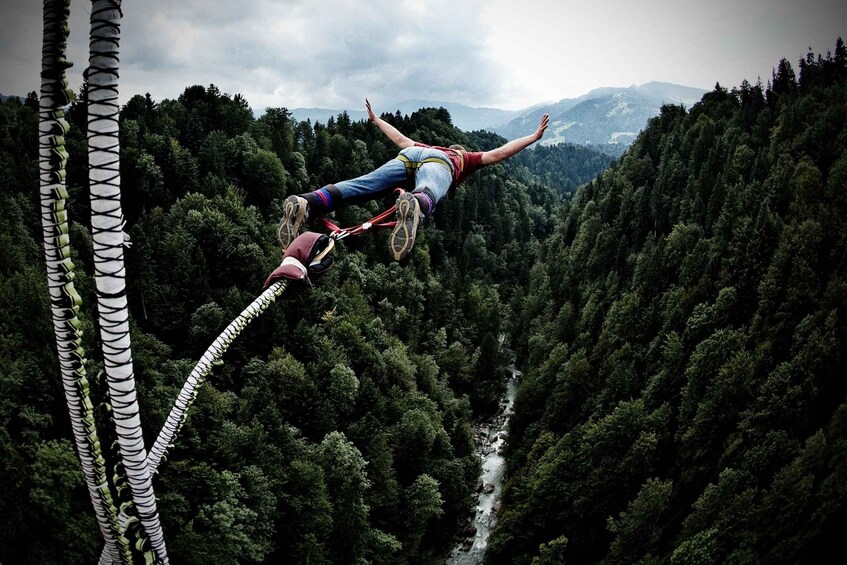 A person bungee jumping with a harness, surrounded by dense forest and a river below. 5