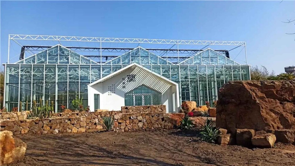 A greenhouse with a white entrance, surrounded by a stone wall and desert plants. 5