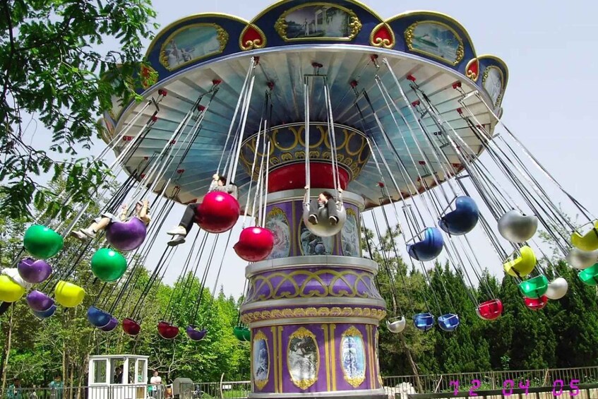 A colorful carousel with multiple seats and a central pole, surrounded by trees. 3