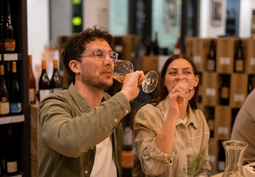 Two people tasting wine in a store with shelves of wine bottles in the background. 3