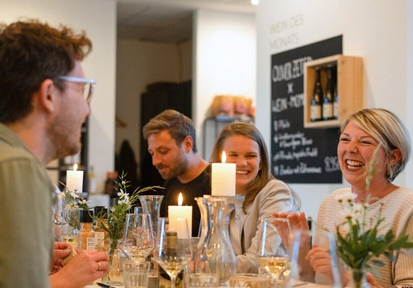 A group of people seated at a table with candles and glassware, in a room with a chalkboard menu. 1