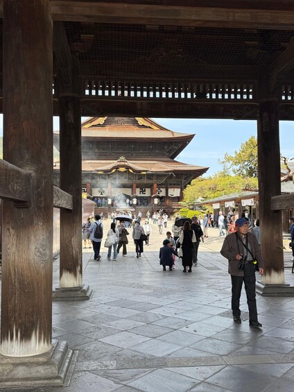 A traditional wooden structure with a tiled roof, surrounded by people walking and standing. 3