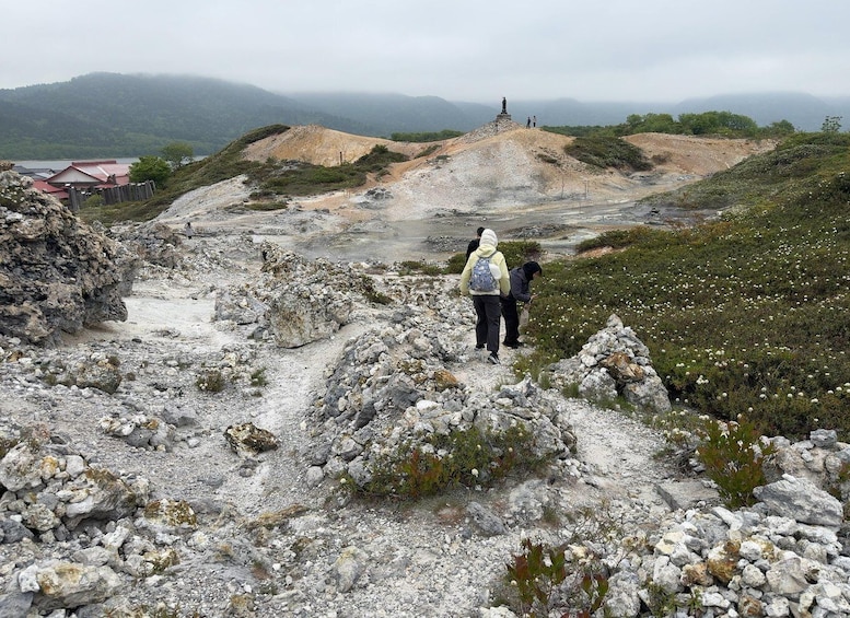 A rocky hiking trail with a statue on a hill, surrounded by sparse vegetation and distant mountains. 1