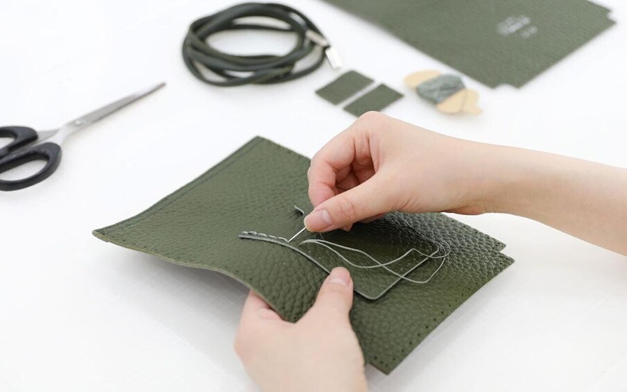 Hands sewing a green fabric with a needle and thread. 1