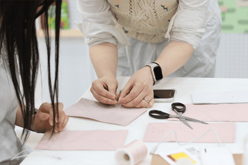 Two people sewing on pink fabric with scissors and thread. 4