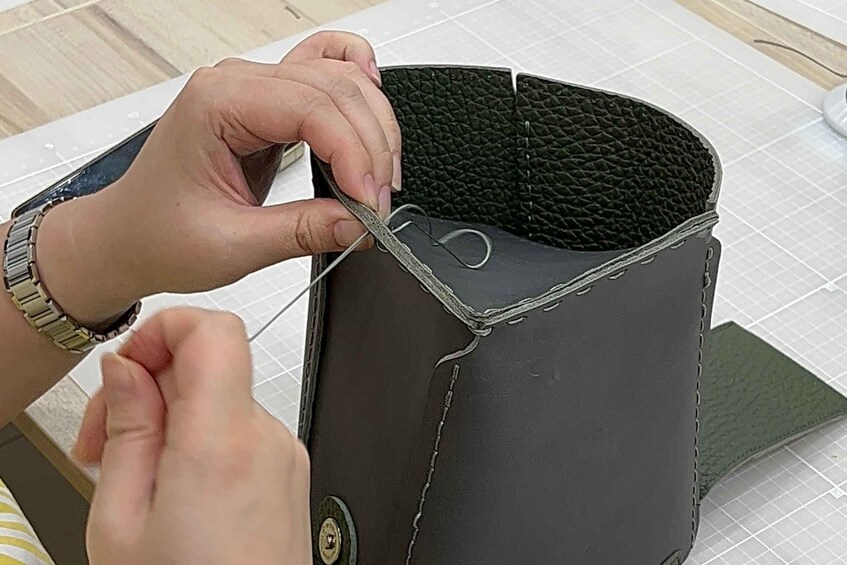 Hands sewing a leather bag with a textured interior. 5