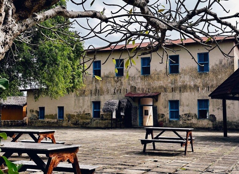 A rustic building with multiple windows and a thatched roof structure in front. 3