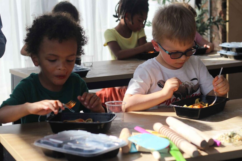 Children eating at a table with bowls of food, a rolling pin, and baking tools. 3