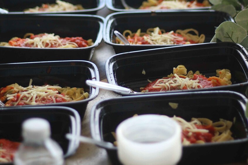 Multiple black containers with pasta dishes topped with cheese and tomato sauce. 4