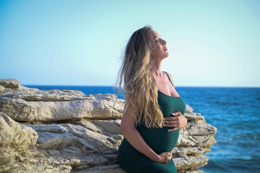 A pregnant woman standing on rocky terrain by the sea. 1