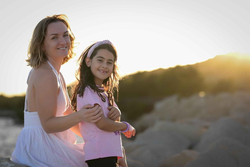 Two people sitting on a rocky beach with a sunset in the background. 4